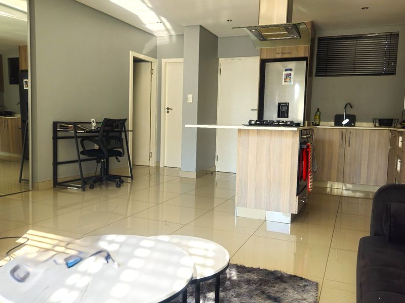 Modern open-plan living area featuring a functional kitchen with a central island, gas hob, extractor fan, and sleek tiled flooring throughout.