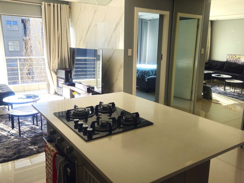 Modern open-plan living area featuring a central kitchen island with a gas hob, sleek finishes, and direct access to a private balcony.