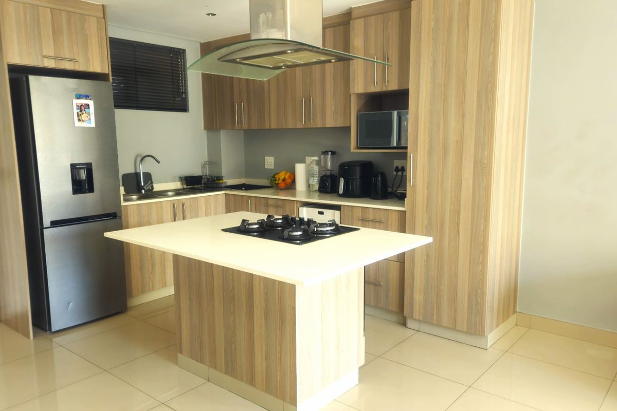 Modern kitchen featuring wood-look cabinetry, a central island with a gas hob, integrated extractor fan, and tiled flooring.