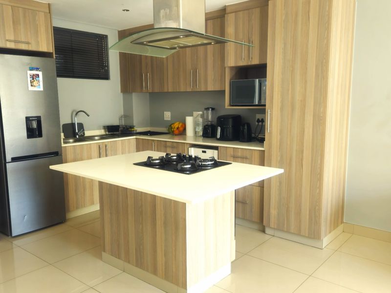 Modern kitchen featuring wood-look cabinetry, a central island with a gas hob, integrated extractor fan, and tiled flooring.