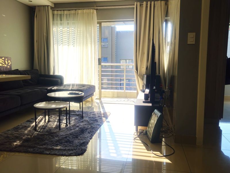 A bright living room featuring large sliding glass doors that open onto a private balcony, with neutral tiled flooring throughout.
