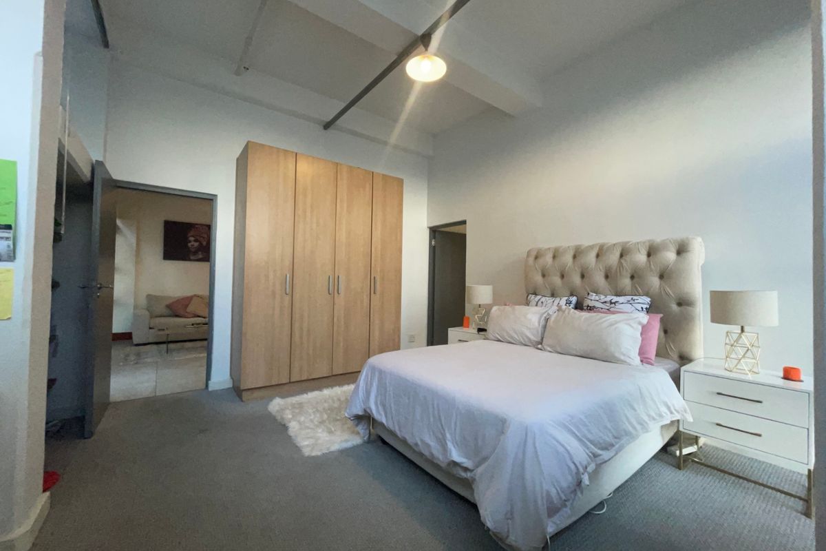 Spacious bedroom featuring high ceilings with exposed beams, neutral carpeting, and a large built-in wardrobe providing ample storage space.