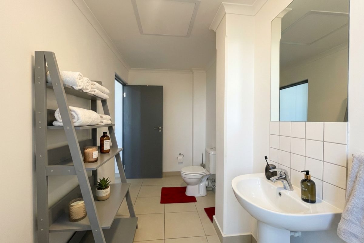 A clean and functional bathroom featuring a pedestal basin, wall-mounted mirror, tiled splashback, and a standard toilet with neutral floor tiling.