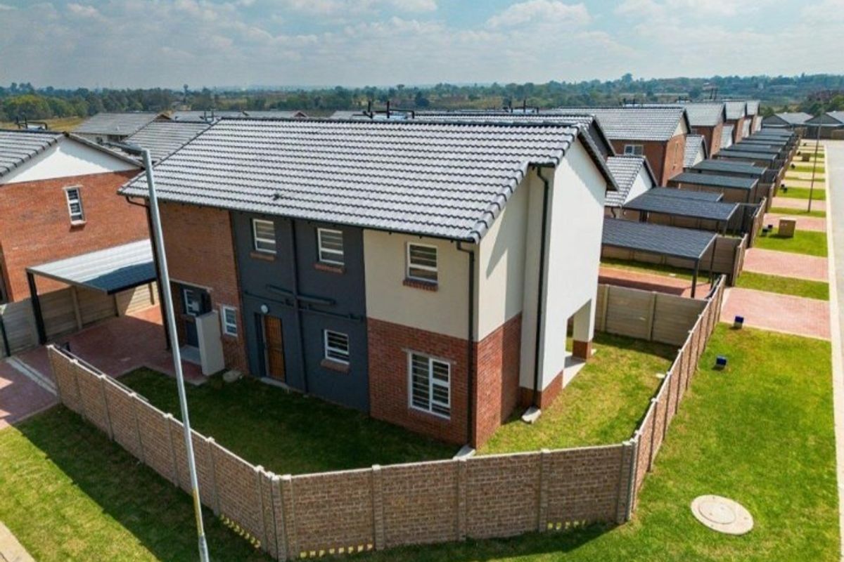 Aerial view of a modern two-story residential property featuring a tiled roof, brick facade, and a private fenced garden with a carport.