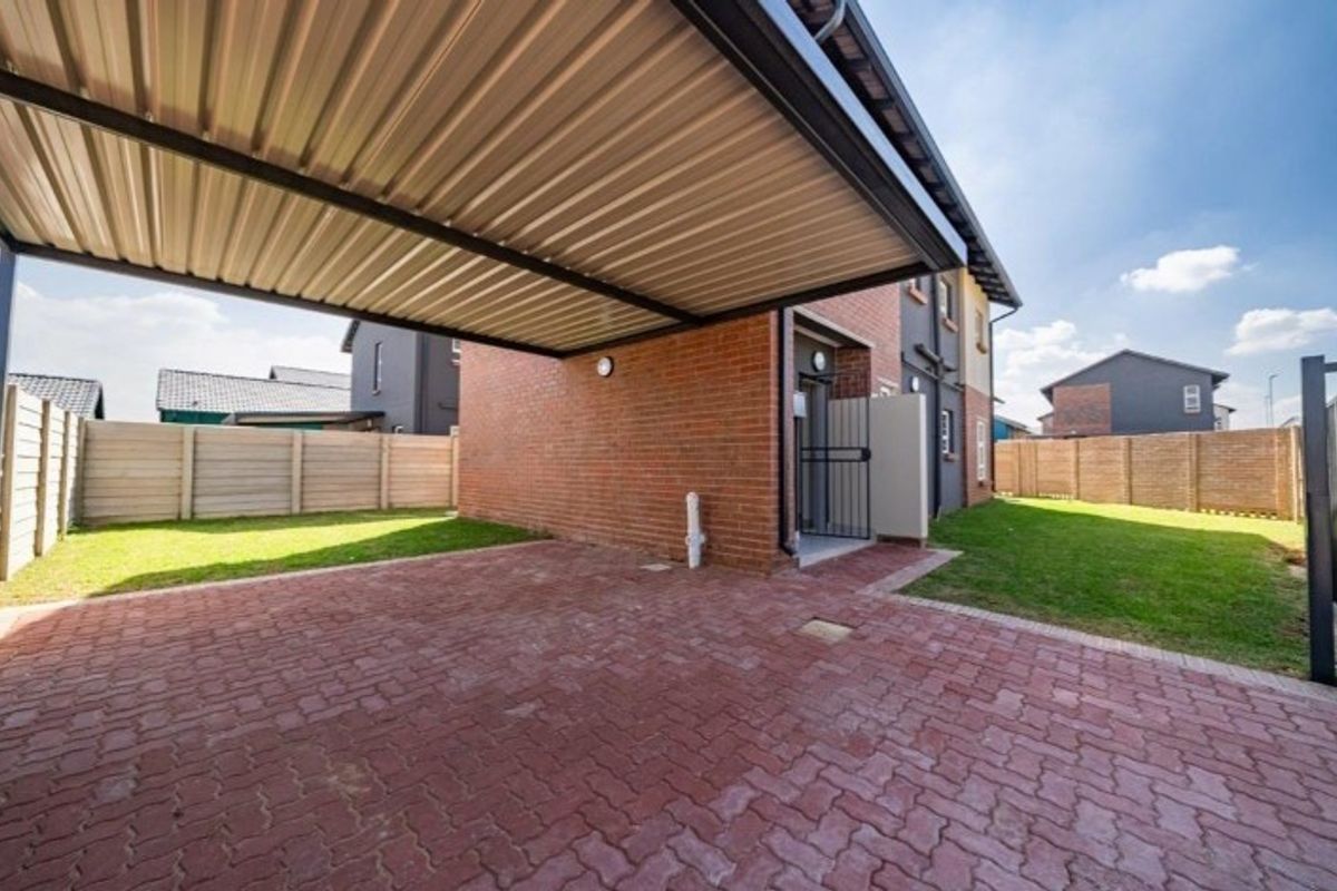 A well-maintained rear exterior area featuring a covered carport, brick-paved driveway, and a private garden enclosed by perimeter fencing.