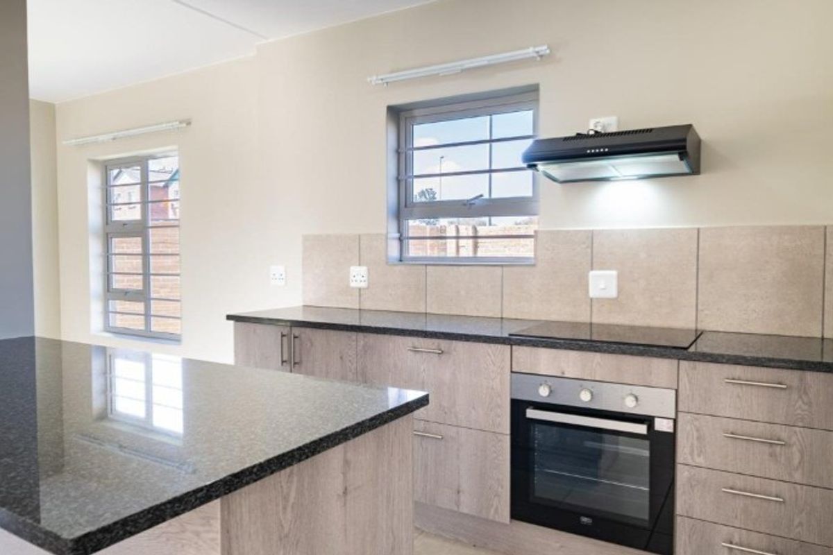 Modern kitchen featuring granite countertops, built-in oven, electric hob, extractor fan, and ample storage cabinetry with a neutral tiled splashback.