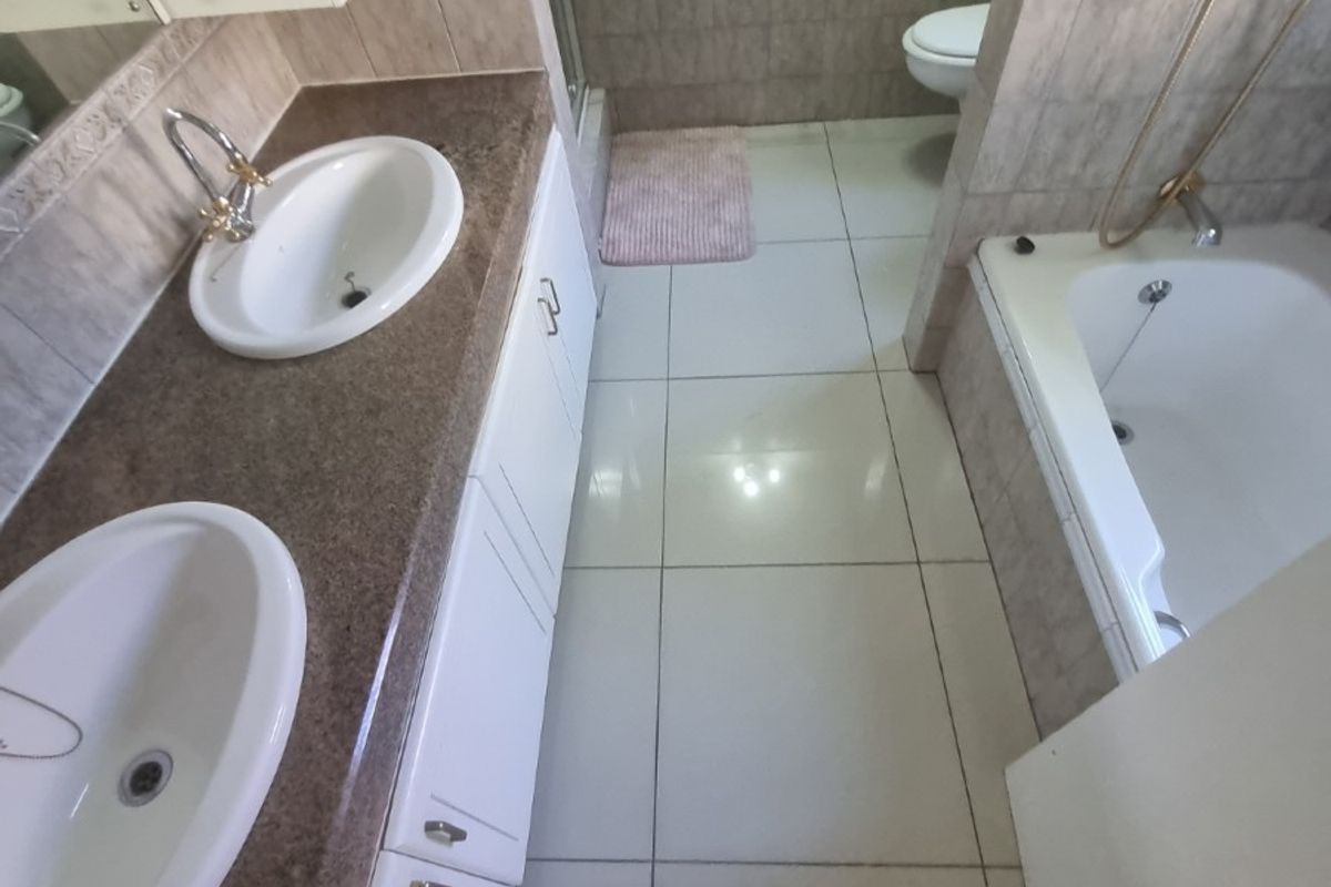 A functional bathroom featuring a double vanity with granite countertop, built-in cabinetry, a separate bathtub, and a shower enclosure with tiled finishes.