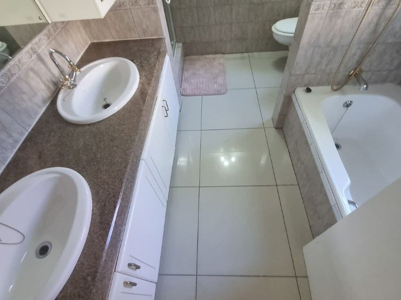 A functional bathroom featuring a double vanity with granite countertop, built-in cabinetry, a separate bathtub, and a shower enclosure with tiled finishes.