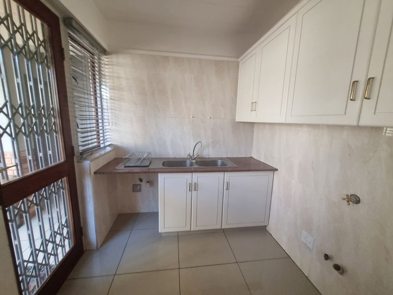 A functional scullery area featuring built-in white cabinetry, a double sink with mixer tap, tiled splashbacks, and tiled flooring with plumbing connections for appliances.