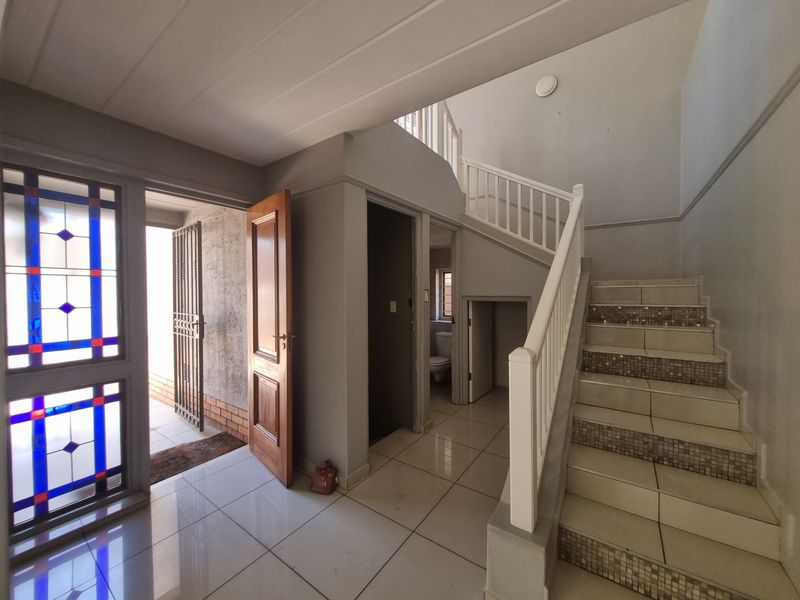 Spacious entrance hall featuring a tiled staircase with balustrade, decorative stained glass window, and direct access to a ground floor guest toilet.