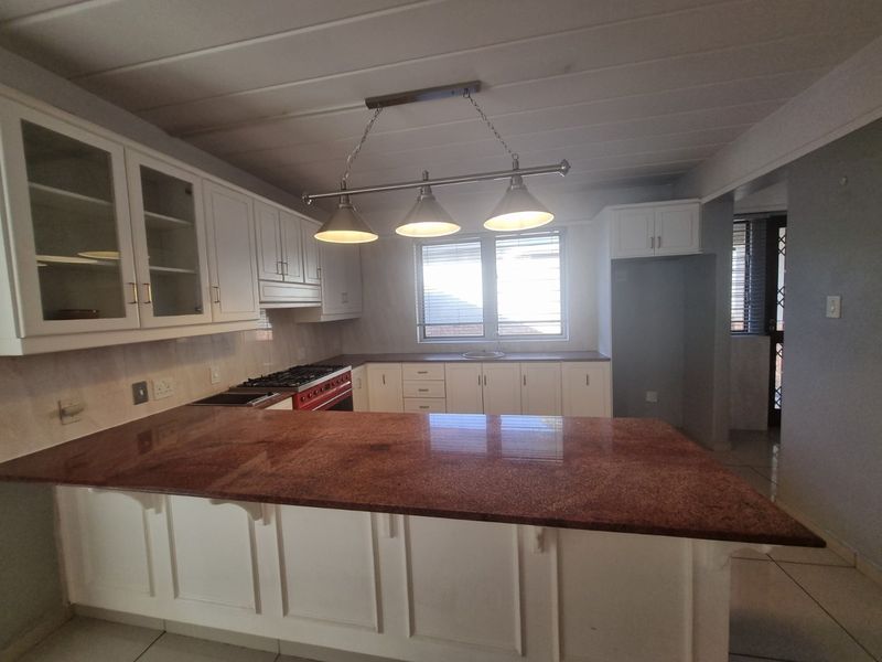 A spacious kitchen featuring white cabinetry, granite countertops, a gas stove, and a central breakfast bar, offering a functional layout with ample storage.