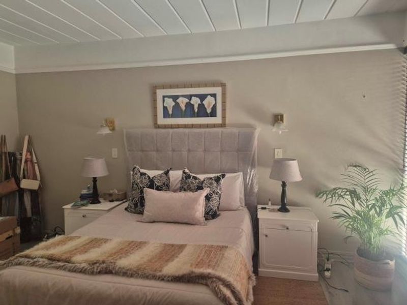 A well-maintained bedroom featuring a neutral color palette, tongue and groove ceiling detail, and wall-mounted lighting fixtures.