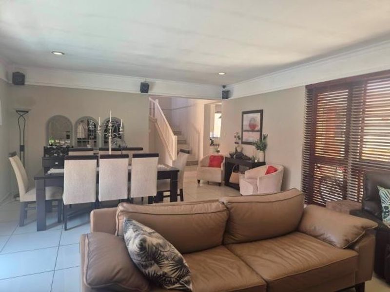 Spacious open-plan living and dining area featuring tiled flooring, recessed lighting, and a staircase leading to the upper level.