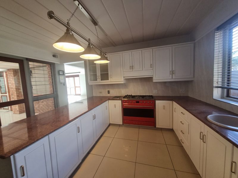 A well-maintained kitchen featuring white cabinetry, granite countertops, a red gas stove, and tiled flooring, offering a clean and functional workspace.