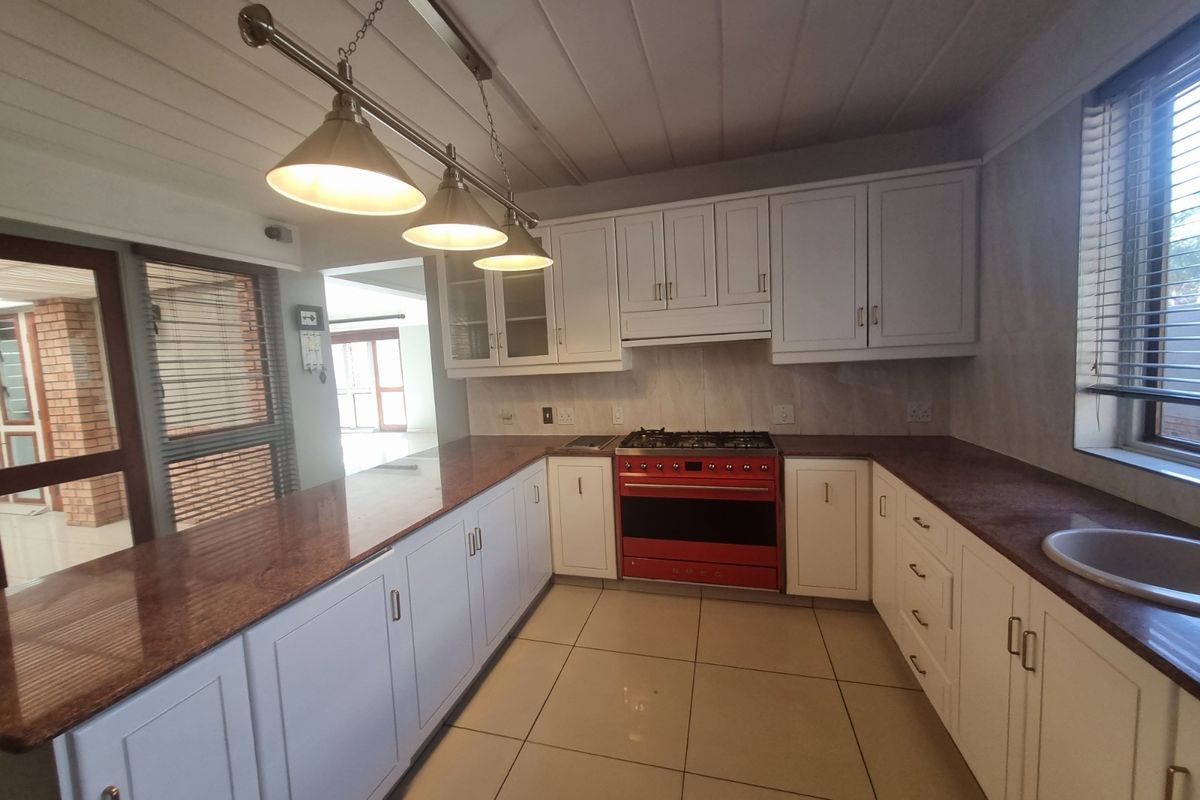 A well-maintained kitchen featuring white cabinetry, granite countertops, a red gas stove, and tiled flooring, offering a clean and functional workspace.