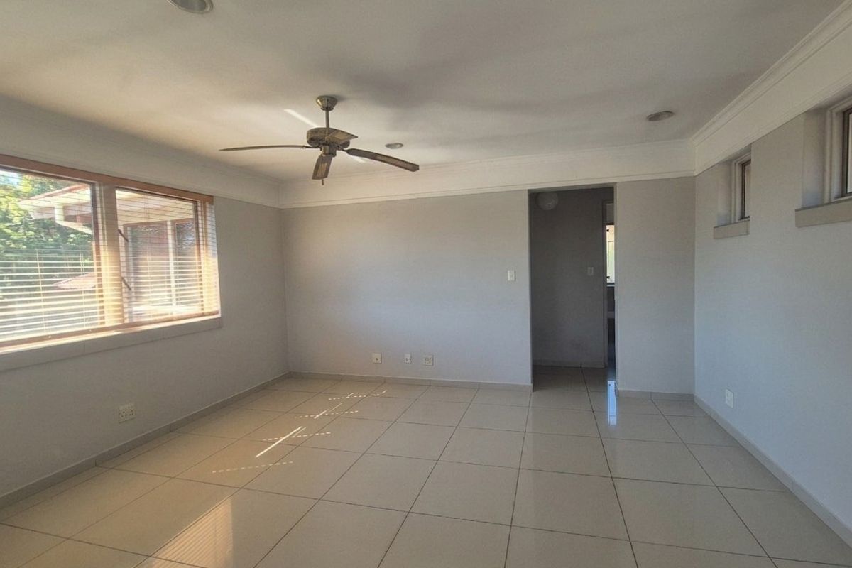A bright, empty living room featuring neutral tiled flooring, recessed lighting, a ceiling fan, and crown molding, offering a clean canvas for personalization.
