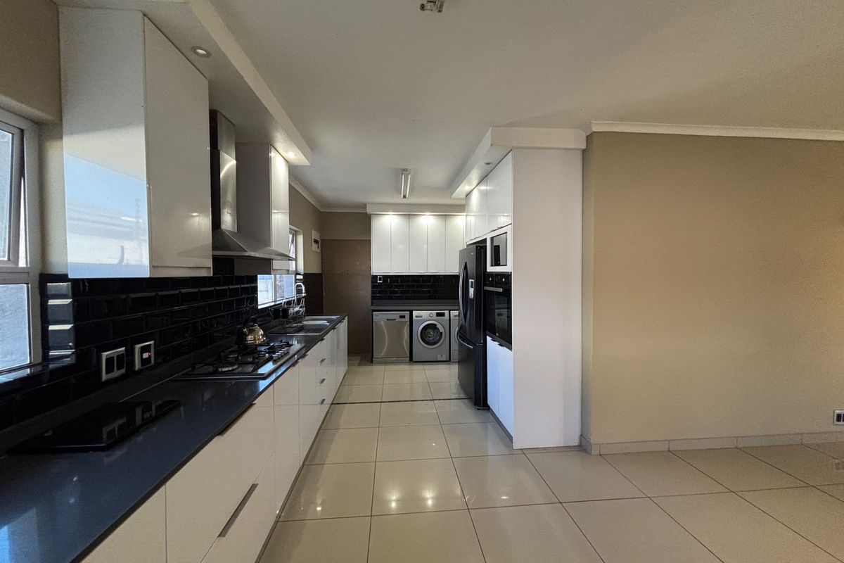 Modern kitchen featuring sleek white cabinetry, dark countertops, subway tile backsplash, and integrated appliances with tiled flooring throughout.