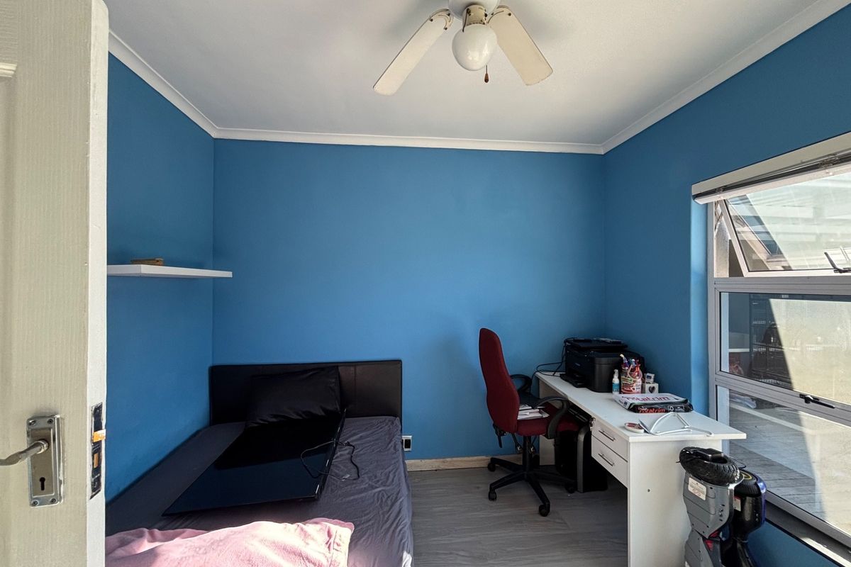 A bedroom featuring laminate flooring, a ceiling fan, and an awning window, currently utilized as a combined sleeping and workspace area.