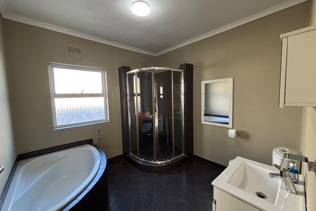A functional bathroom featuring a corner bathtub, separate shower enclosure, vanity basin, and toilet with dark tiled flooring.
