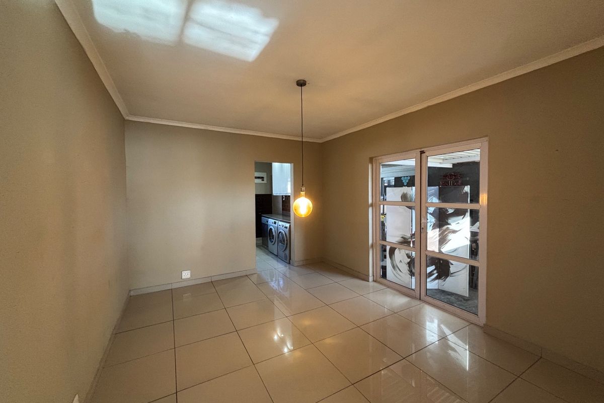 An empty living area featuring neutral tiled flooring, coved ceilings, and sliding glass doors leading to an adjacent space.