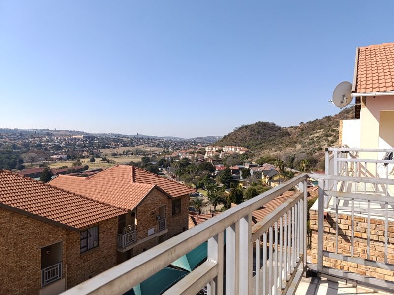 Elevated view from a balcony overlooking the surrounding residential estate and landscape, featuring a metal safety railing and clear horizon.