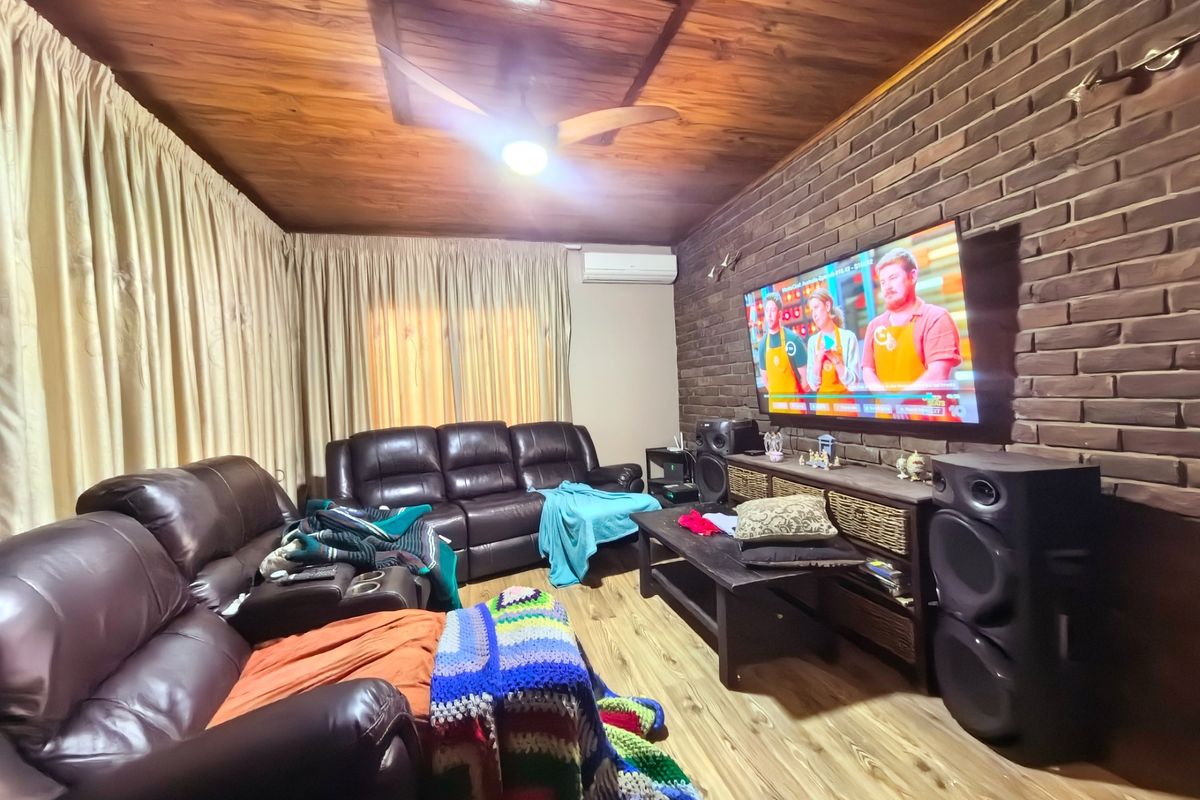 A cozy living room featuring a rustic exposed brick wall, warm timber ceiling, laminate flooring, and a wall-mounted air conditioning unit.