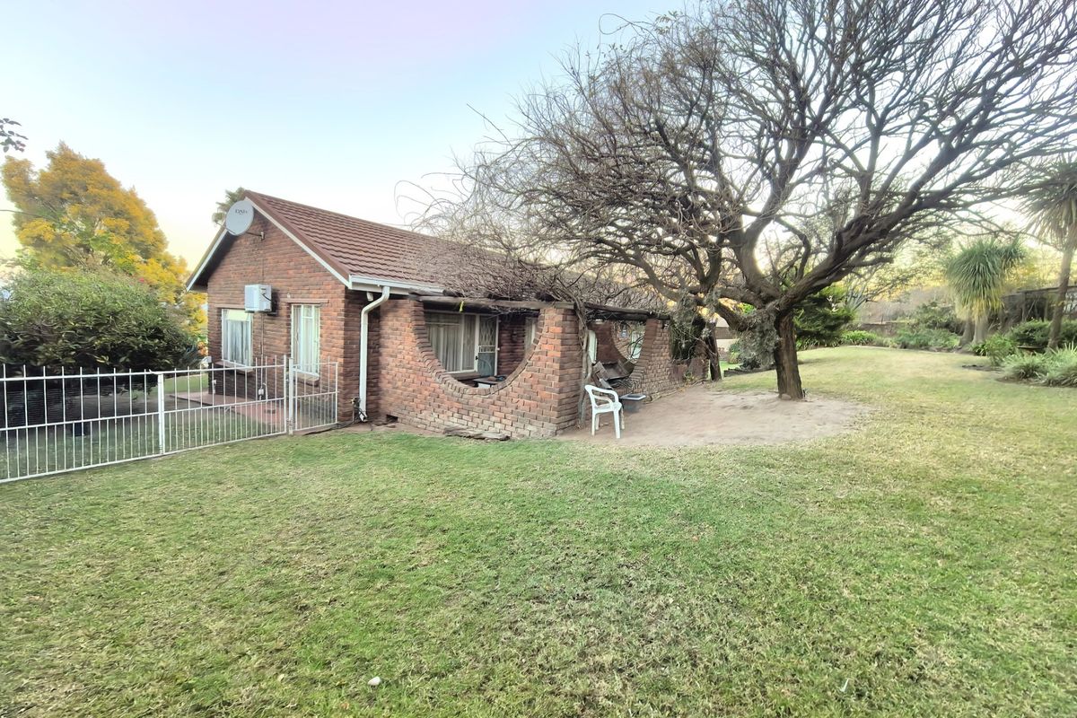Rear view of a brick house featuring a covered patio with distinctive brick archways, set within a spacious garden with mature trees.