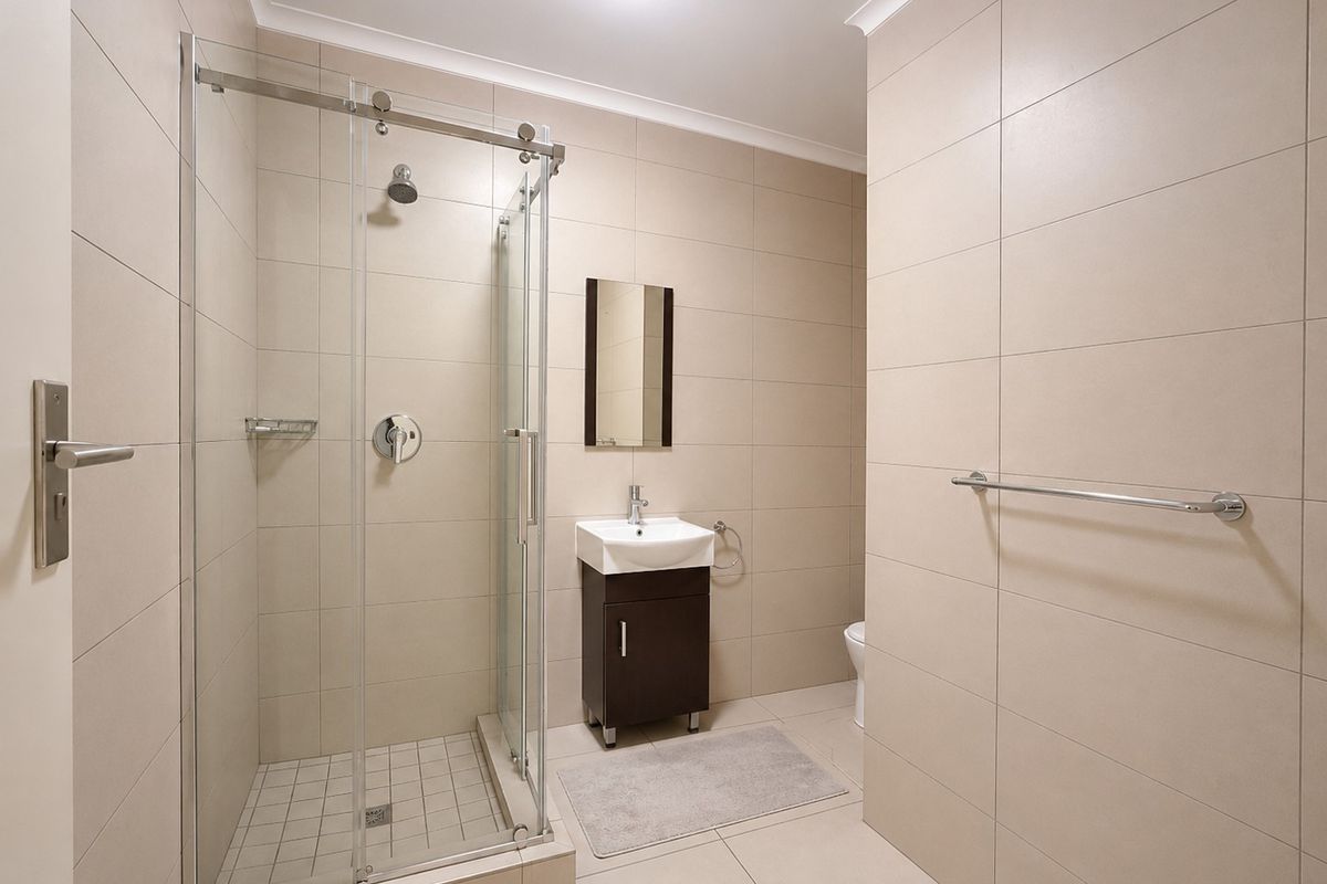 Modern bathroom featuring a glass-enclosed shower, vanity cabinet with basin, and neutral floor-to-ceiling ceramic tiling.