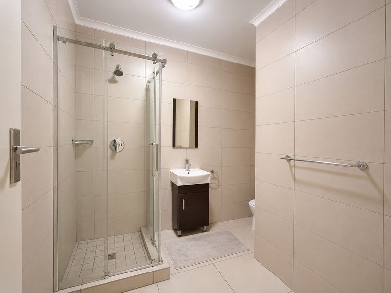 Modern bathroom featuring a glass-enclosed shower, vanity cabinet with basin, and neutral floor-to-ceiling ceramic tiling.