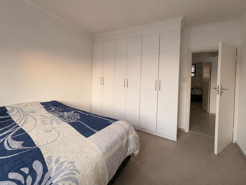 A well-maintained bedroom featuring neutral carpeted flooring, white walls, and extensive built-in cupboard storage with modern handles.