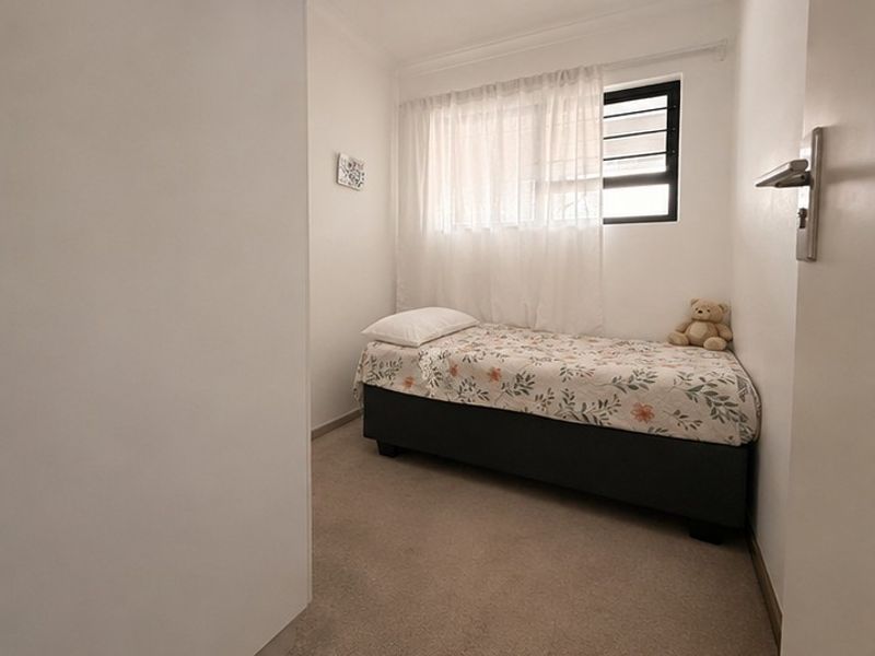 A compact bedroom featuring neutral carpeted flooring and a window fitted with security burglar bars.