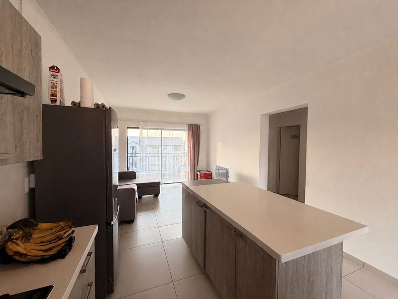 Open-plan living area featuring a modern kitchen island, tiled flooring, and a sliding glass door leading to a balcony.
