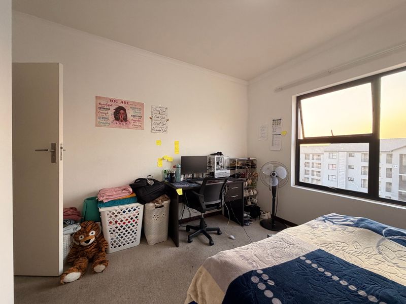 A functional bedroom featuring carpeted flooring and a large window with views of the surrounding apartment complex.