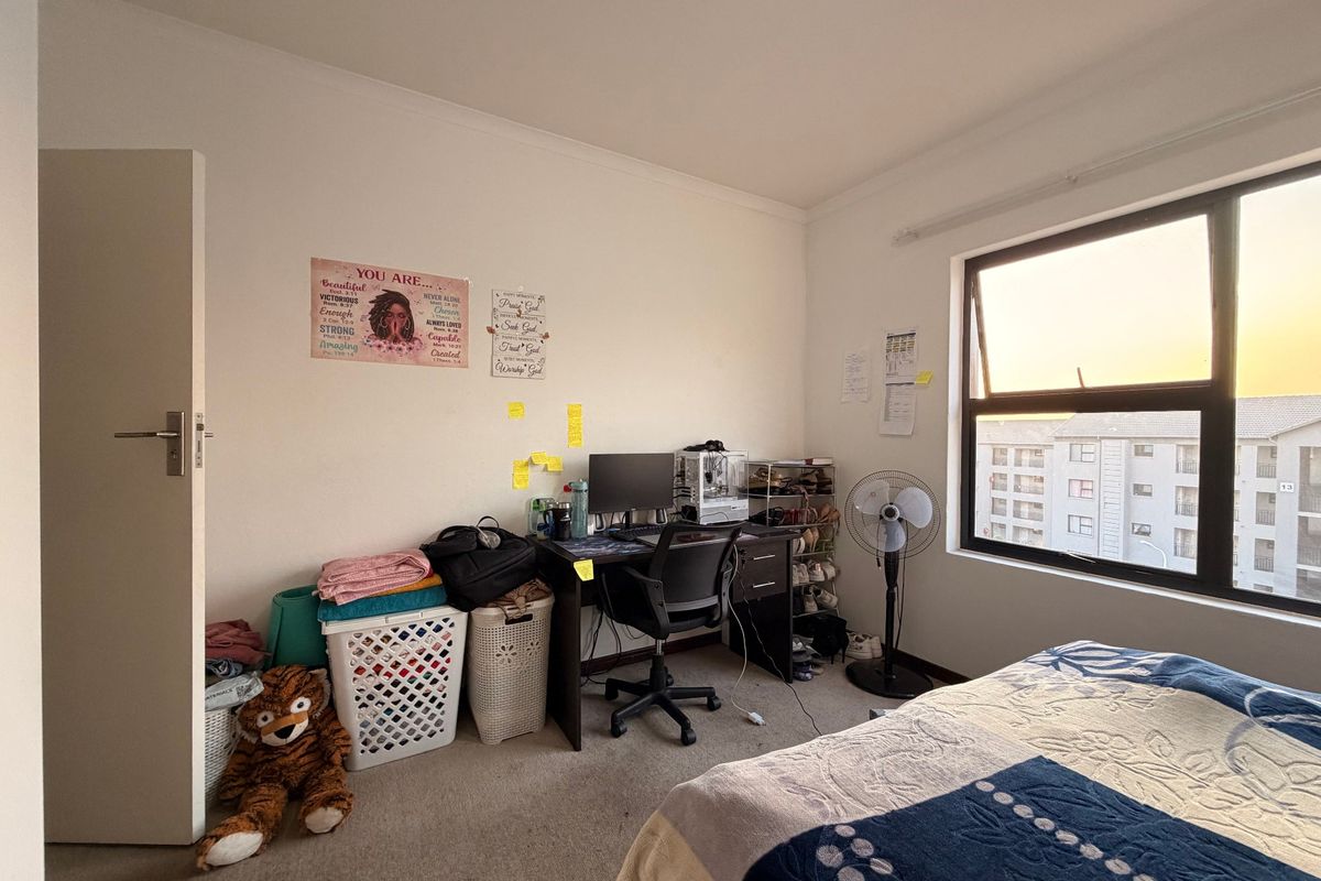 A functional bedroom featuring carpeted flooring and a large window with views of the surrounding apartment complex.