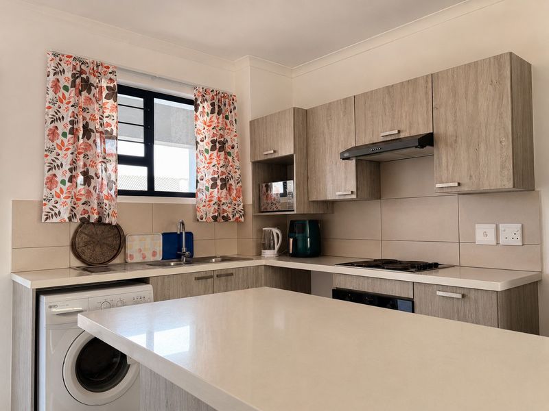 A modern kitchen featuring light wood-grain cabinetry, stone countertops, a built-in hob, extractor fan, and integrated space for a washing machine.