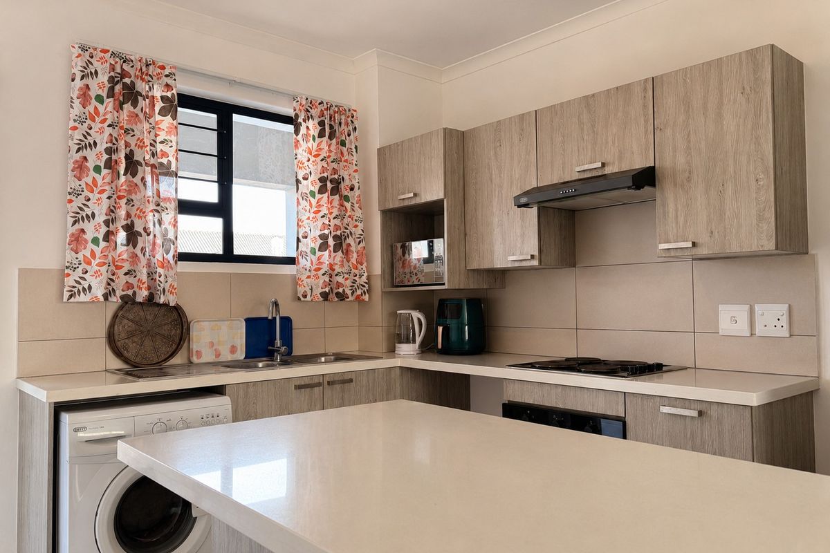 A modern kitchen featuring light wood-grain cabinetry, stone countertops, a built-in hob, extractor fan, and integrated space for a washing machine.