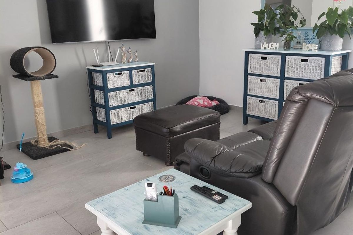 A comfortable living room featuring neutral tiled flooring and a wall-mounted television, providing a functional and well-maintained space.