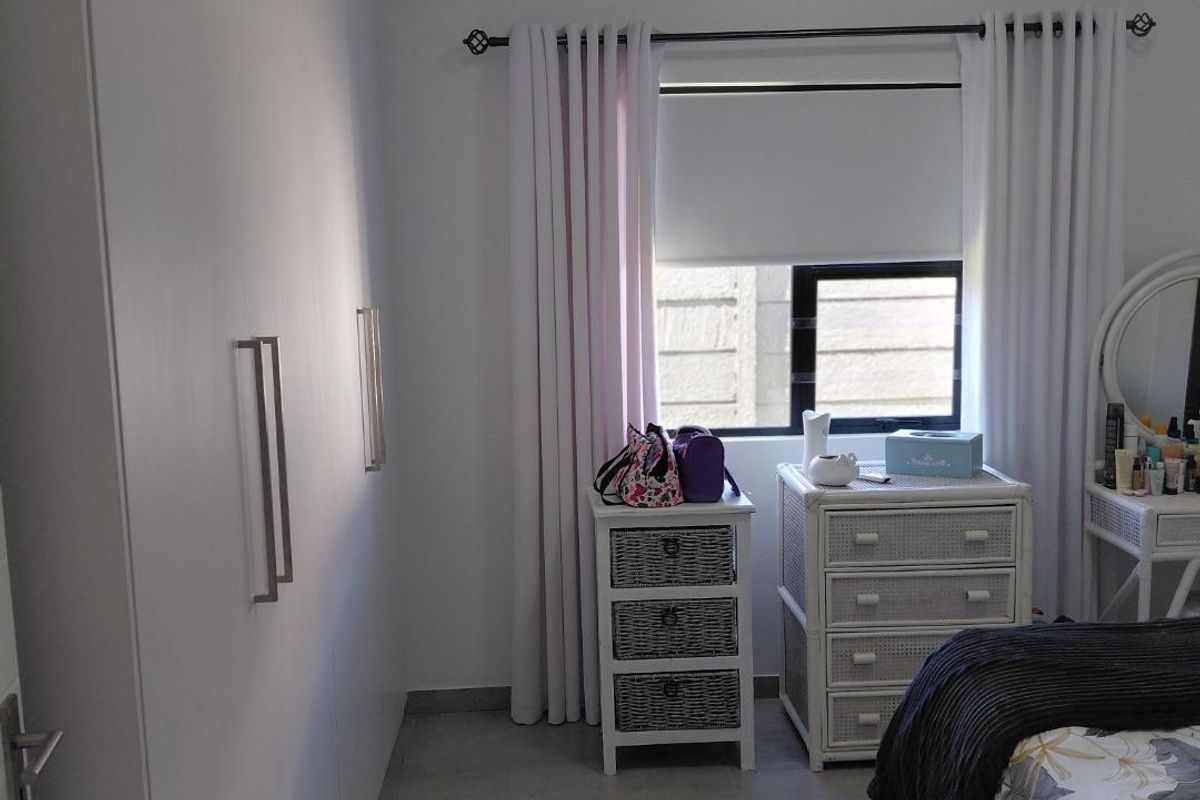 A well-maintained bedroom featuring neutral tiled flooring, a large built-in wardrobe, and a wall-mounted split-system air conditioning unit.