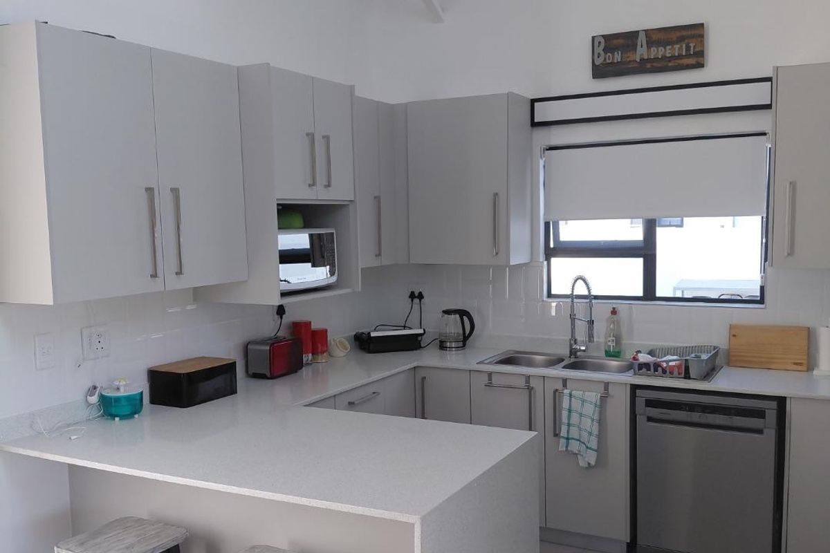 Modern kitchen featuring light grey cabinetry, stone countertops, subway tile backsplash, and a vaulted ceiling with exposed rafters, creating a bright and airy space.