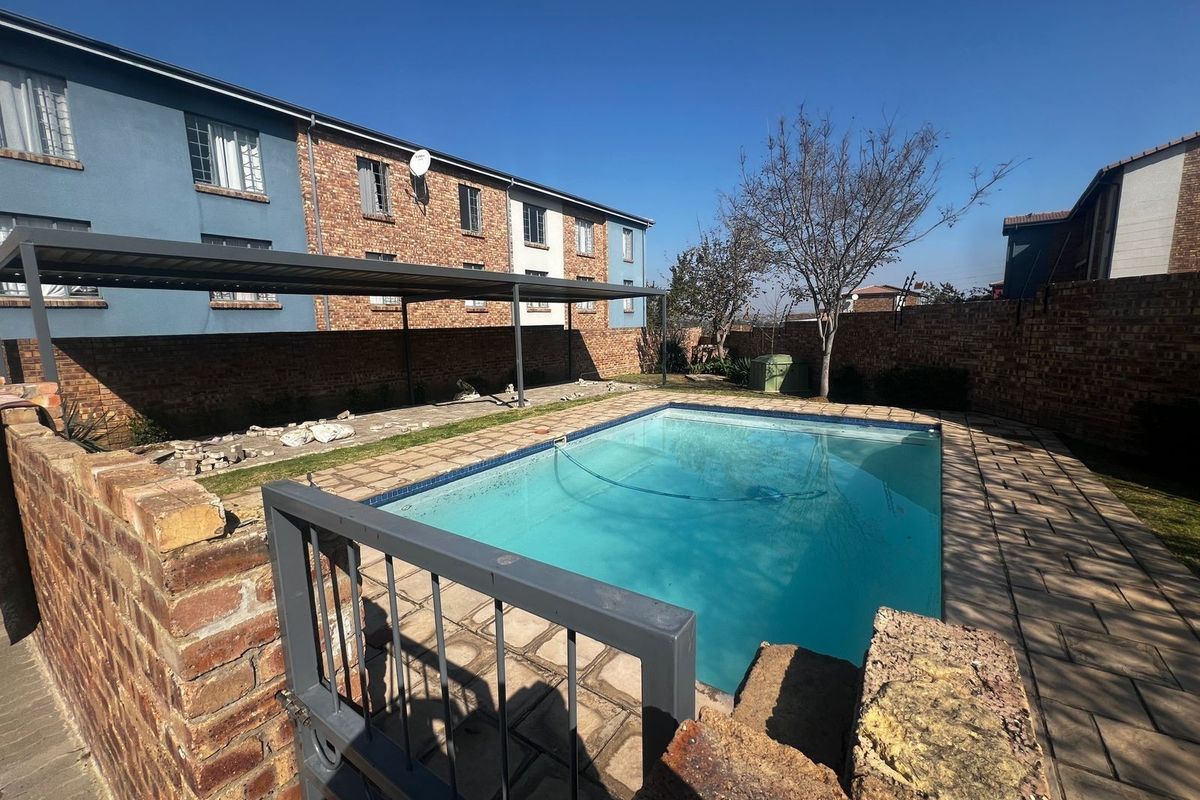 Outdoor pool area featuring a paved surround, metal carport, and brick boundary wall, providing a functional space for recreation.