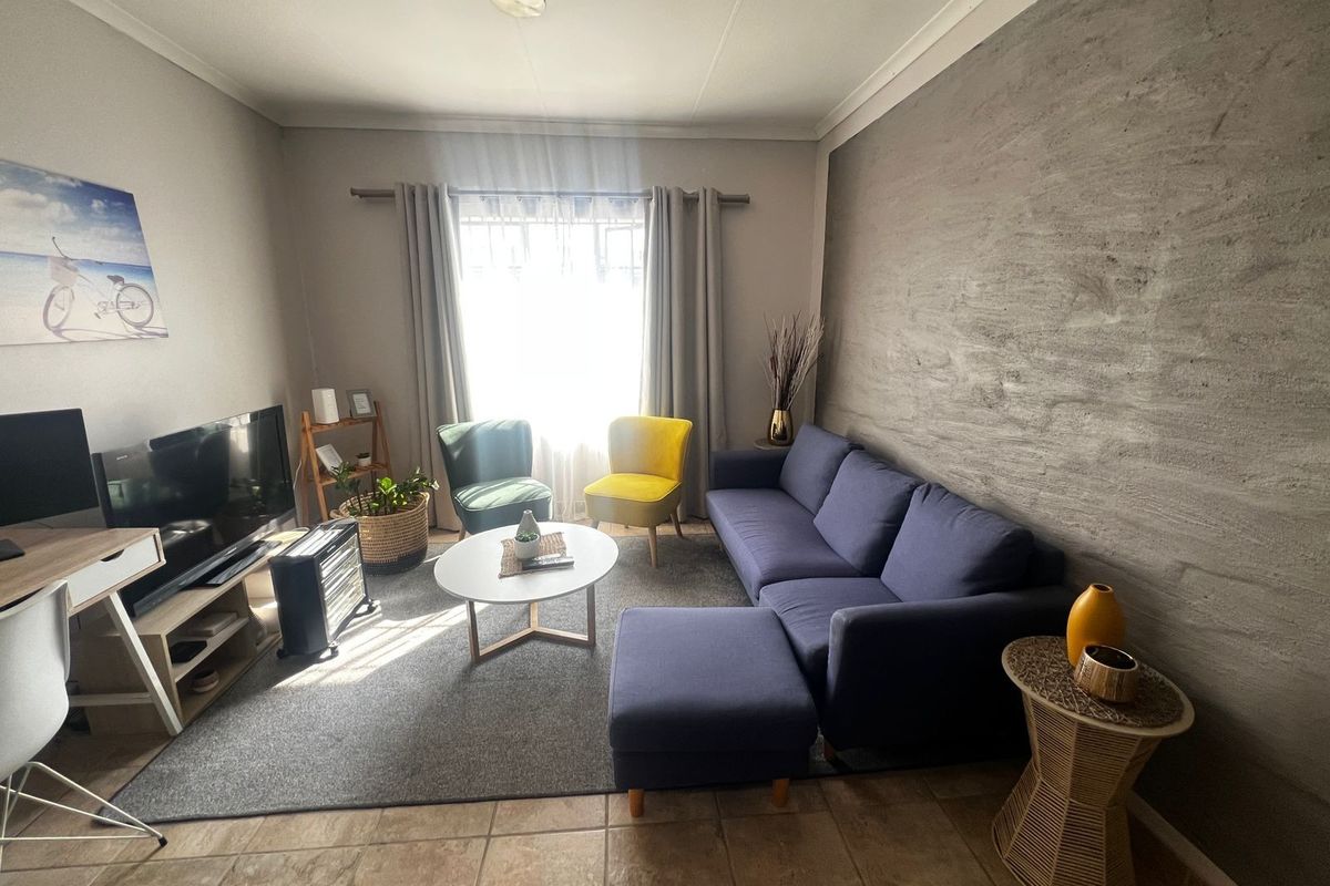 A comfortable living room featuring a textured accent wall, tiled flooring, and natural light through a window with curtain treatments.