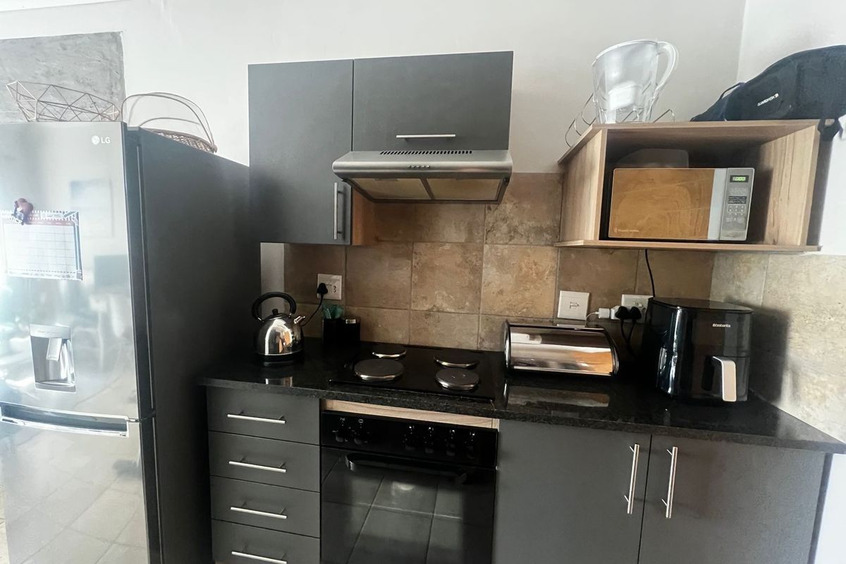 A compact kitchen featuring modern grey cabinetry, granite countertops, a built-in oven, electric hob, and a tiled backsplash.