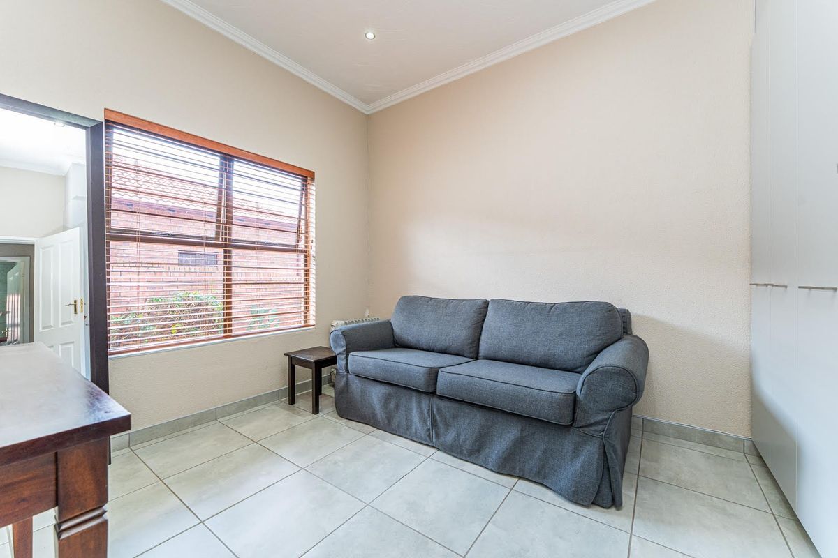 A well-maintained living room featuring neutral tiled flooring, built-in storage cupboards, and natural light through a window with fitted blinds.