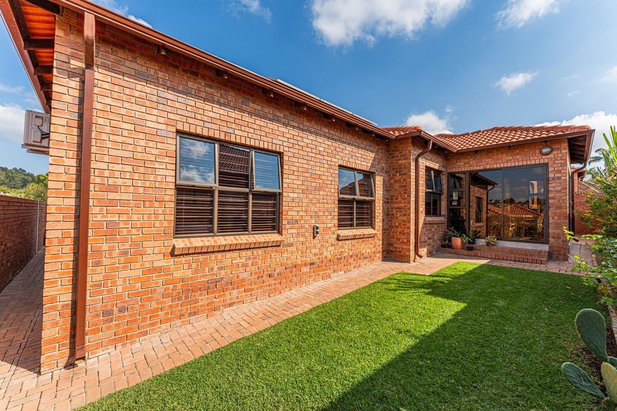 A well-maintained rear exterior view of the townhouse featuring face brick walls, a tiled roof, and a paved walkway leading to a small garden.