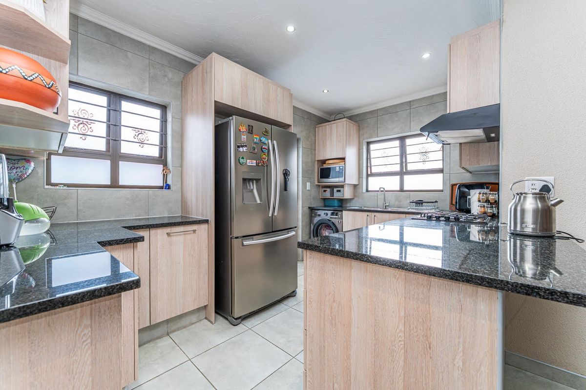 Modern kitchen featuring light wood cabinetry, granite countertops, a gas hob, extractor fan, and tiled flooring with integrated laundry space.