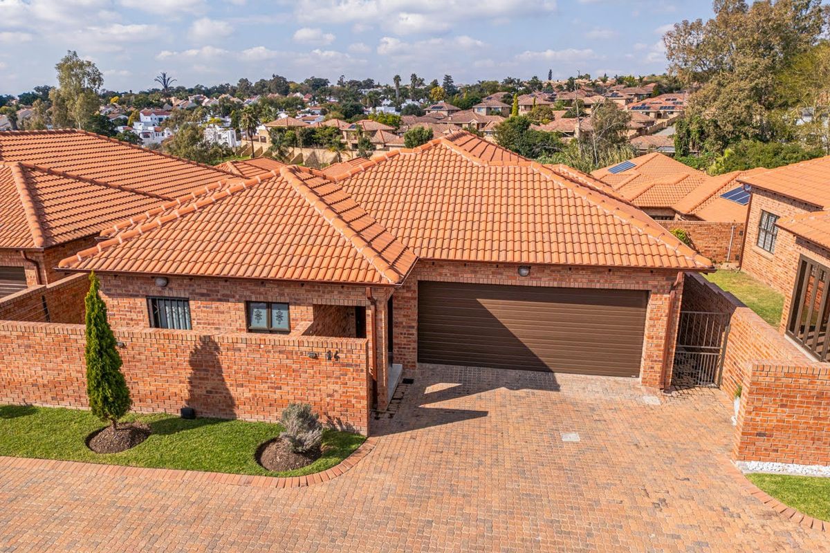 Aerial view of a brick townhouse featuring a tiled roof, paved driveway, and a double garage, situated within a residential complex.