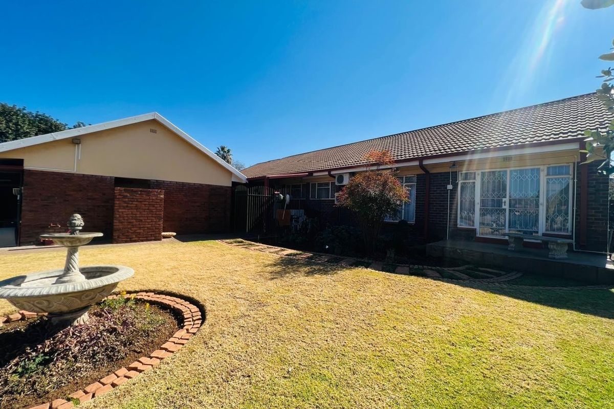 Rear view of the property featuring a well-maintained lawn, a decorative stone fountain, brick garden borders, and a tiled roof structure.