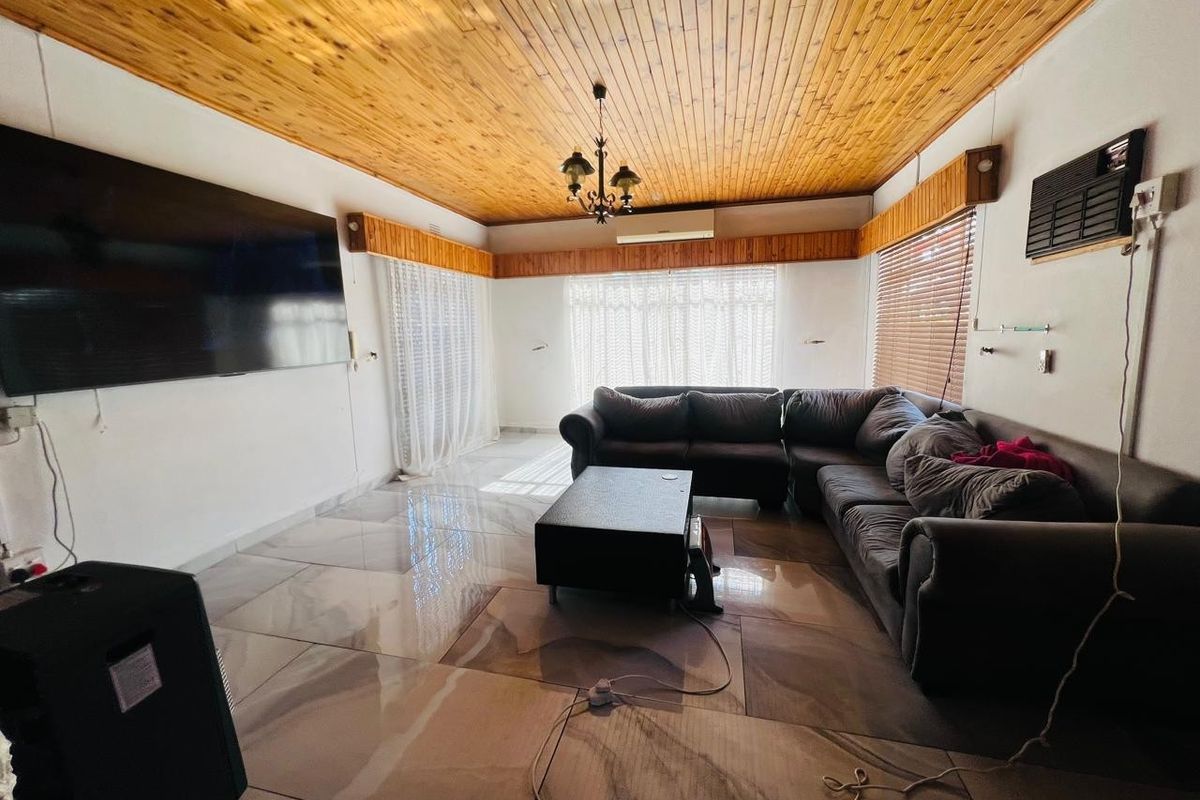 Spacious living room featuring large format floor tiles, a distinctive timber tongue and groove ceiling, and a wall-mounted air conditioning unit.