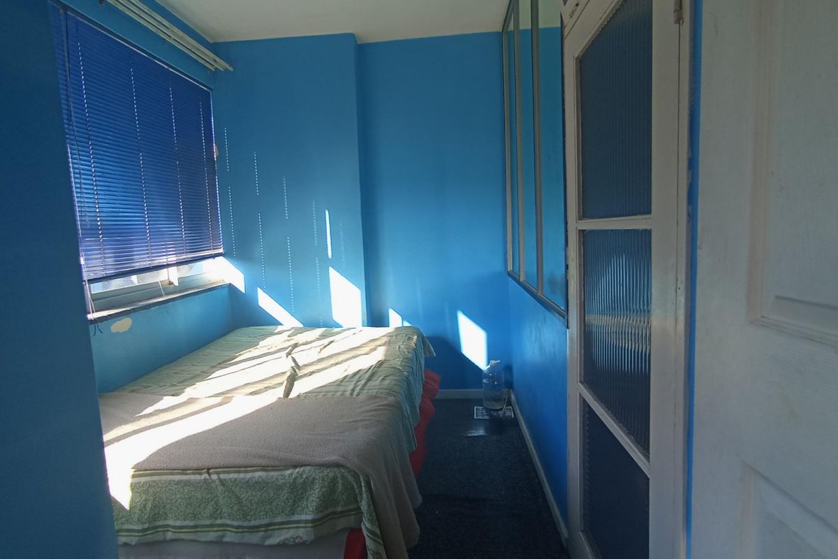 A bedroom featuring blue walls, mirrored wall panels, a fluted glass door, and venetian blinds.