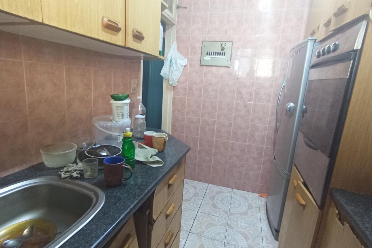 A compact kitchen featuring dated cabinetry, ceramic wall and floor tiles, a built-in oven, and a stainless steel sink.